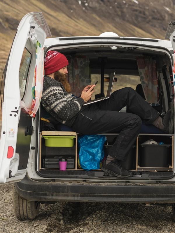 a man is sitting in the back of a campervan in iceland looking at his phone .