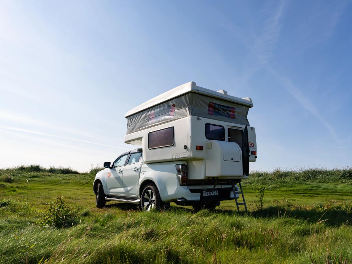 Camper Rear Three-Quarter View Rear view of the camper on grass, roof raised and steps lowered, 4x4 campervan rental Iceland