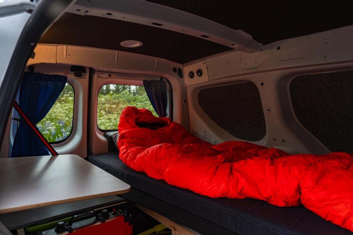 Roter Schlafsack auf dem Bett neben einem kleinen Tisch, mit Blick auf die hinteren Fenster