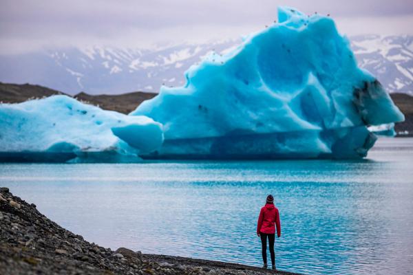 a woman with a red jacket admiring and iceberg in a glacier lagoon