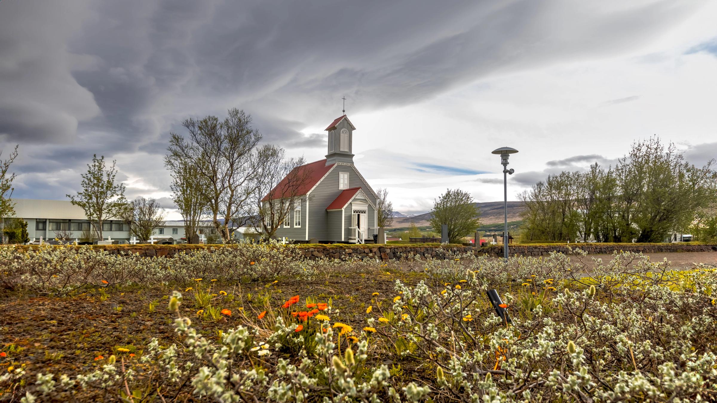 una pequeña iglesia con techo rojo está rodeada por un campo de flores .