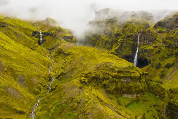 an aerial view of a waterfall in the middle of a lush green mountain valley .