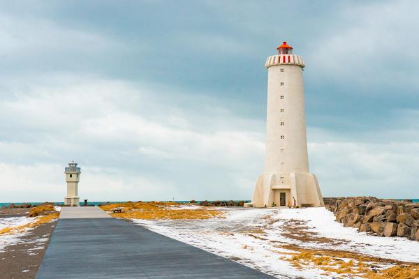 A large white lighthouse with a red top and a smaller lighthouse stand on a snow-dusted coast with a path.