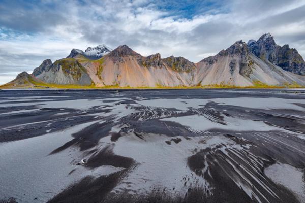 a mountain with black and grey volcanic sand on the foreground