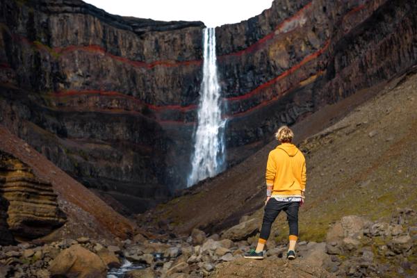 un hombre con una sudadera amarilla está parado frente a una cascada.
