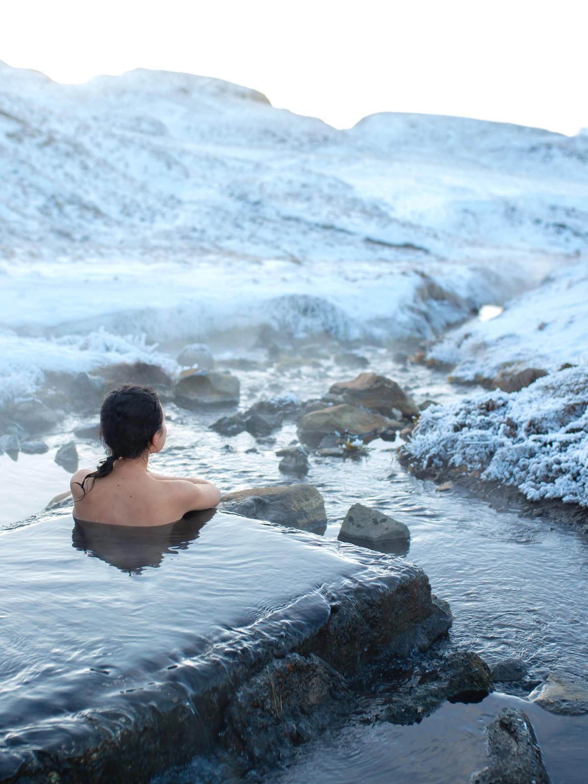a woman is taking a bath in a hot spring in the snow .