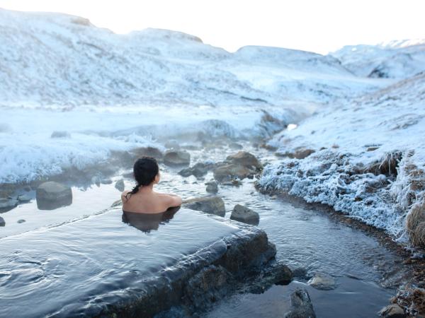 Woman soaking in a natural hot spring surrounded by snowy landscapes in Iceland.