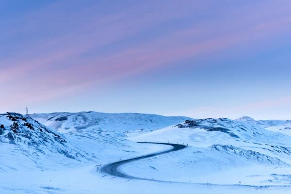 snowy road in Iceland a snowy mountain with a road going through it .