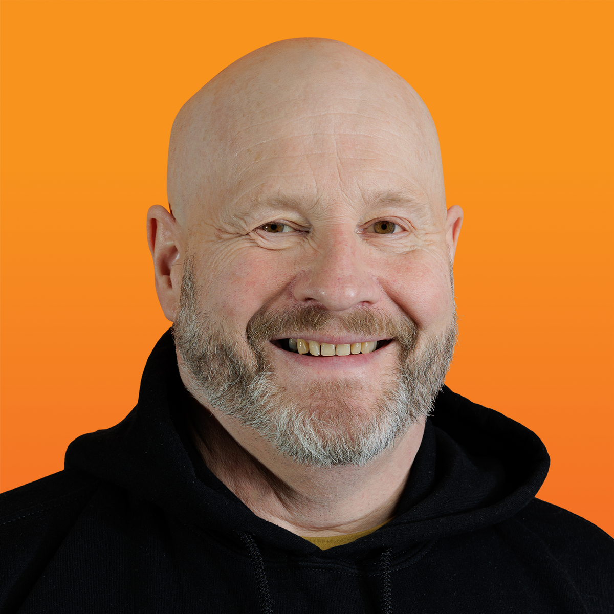 a smiling bald man with a beard wearing a black hoodie