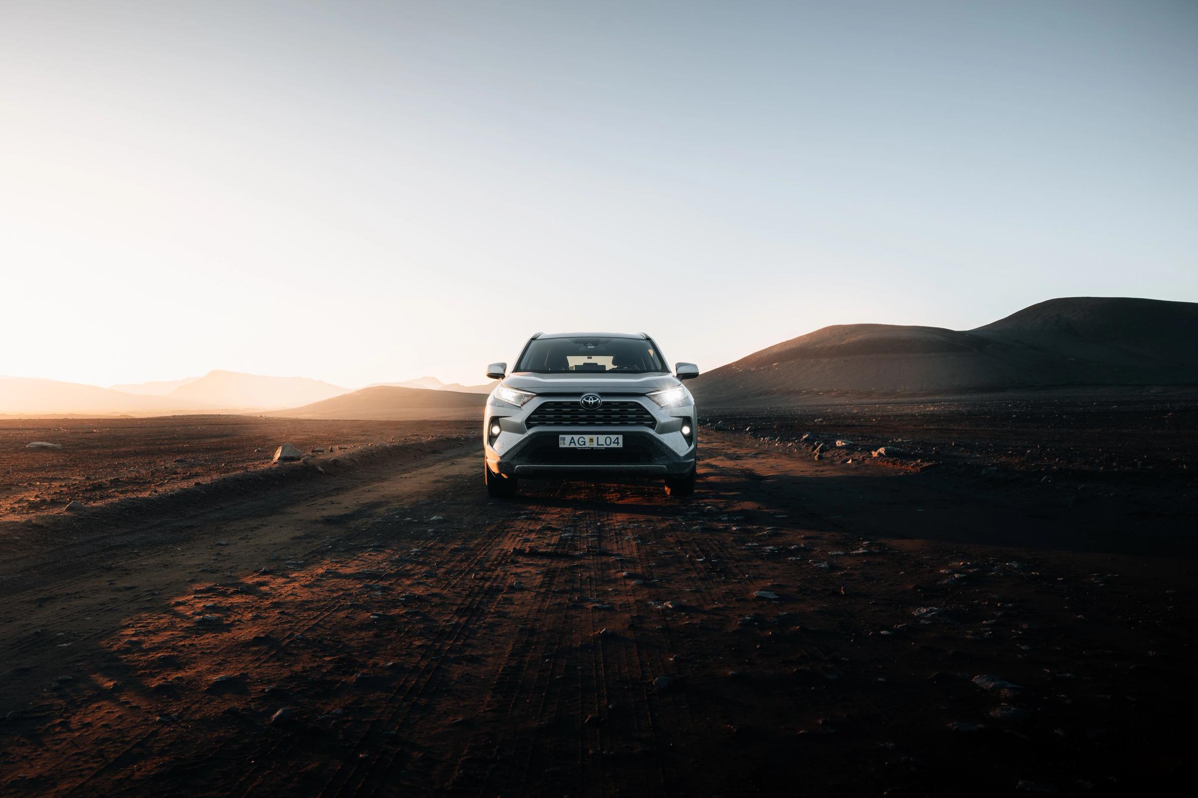 Toyota RAV4 SUV rental Iceland facing forward on a gravel track in open highland landscape