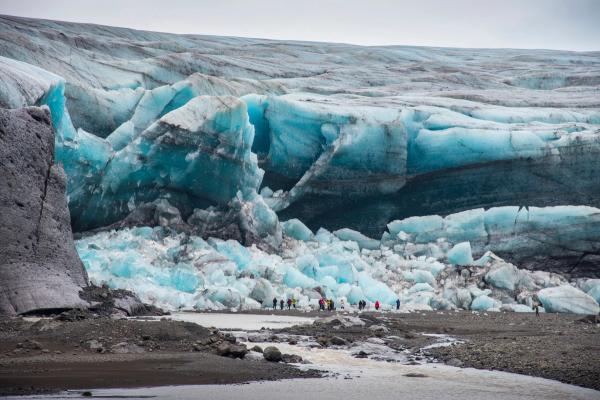 a group of people are standing in front of a large glacier .