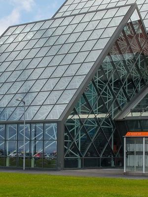 a large glass building with a red roof is sitting on top of a lush green field .