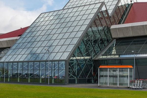 Modern airport terminal with a prominent glass facade, red roof, and green lawn.