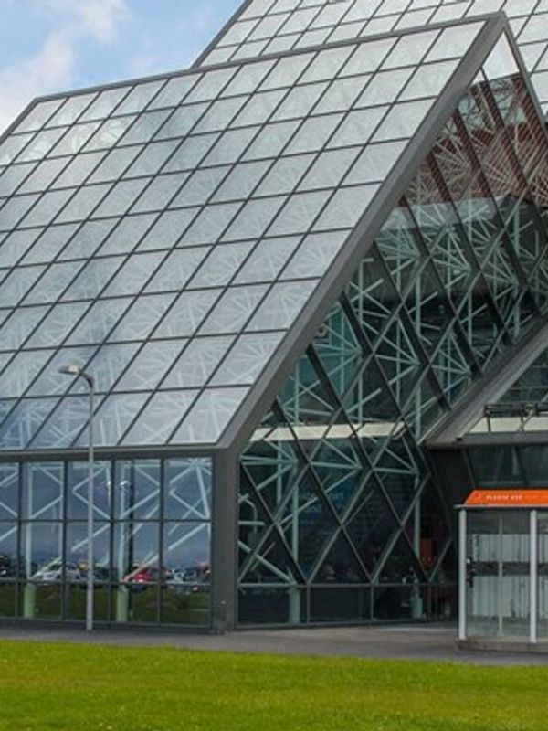 a large glass building with a red roof is sitting on top of a lush green field .