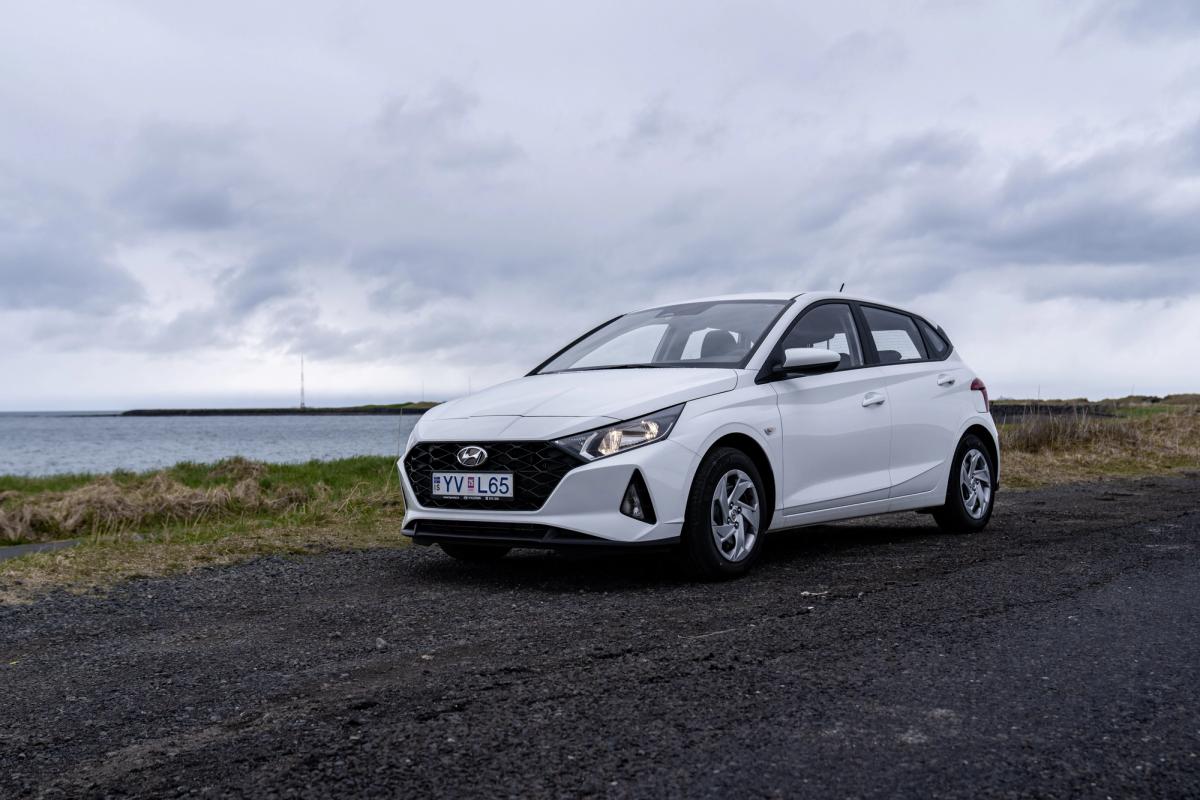 White Hyundai i20 on a gravel road by the sea under a cloudy sky.