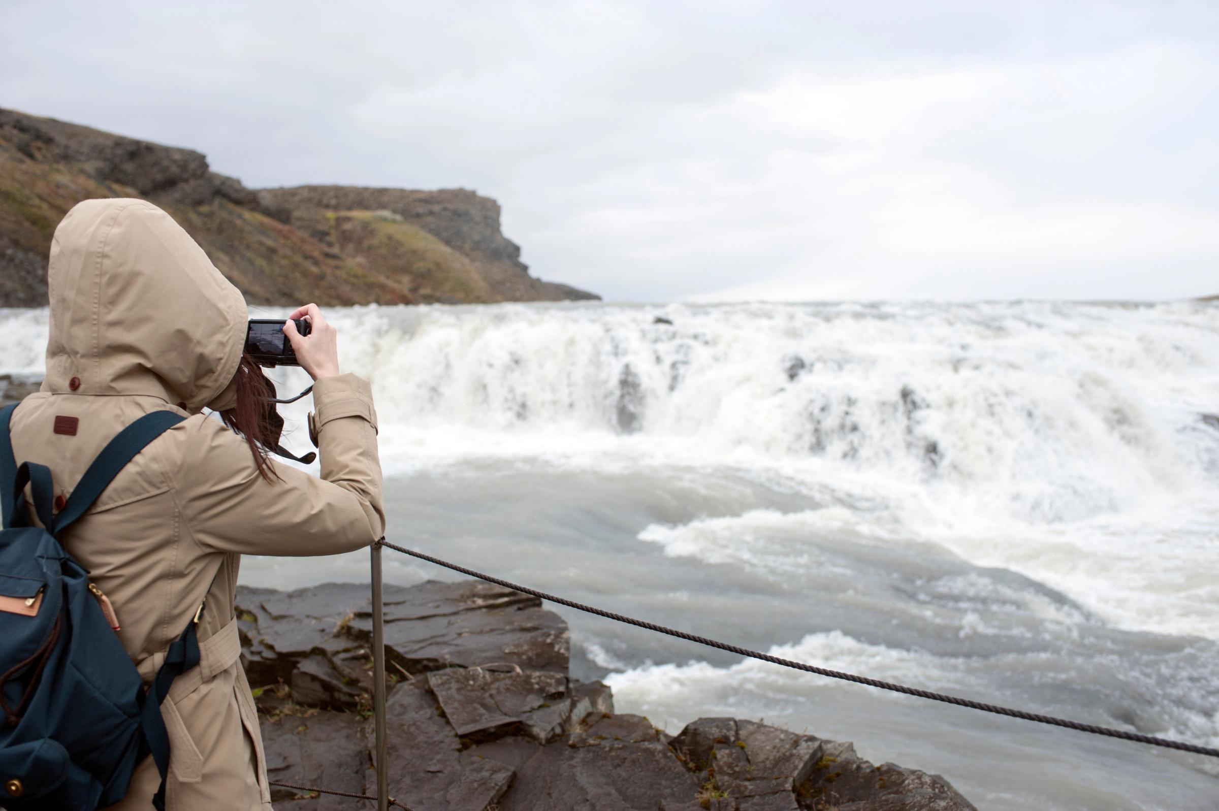 a woman with a beige jacket taking pictures of a waterfall