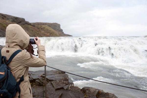 una mujer con una chaqueta de color beige haciendo fotos de una cascada