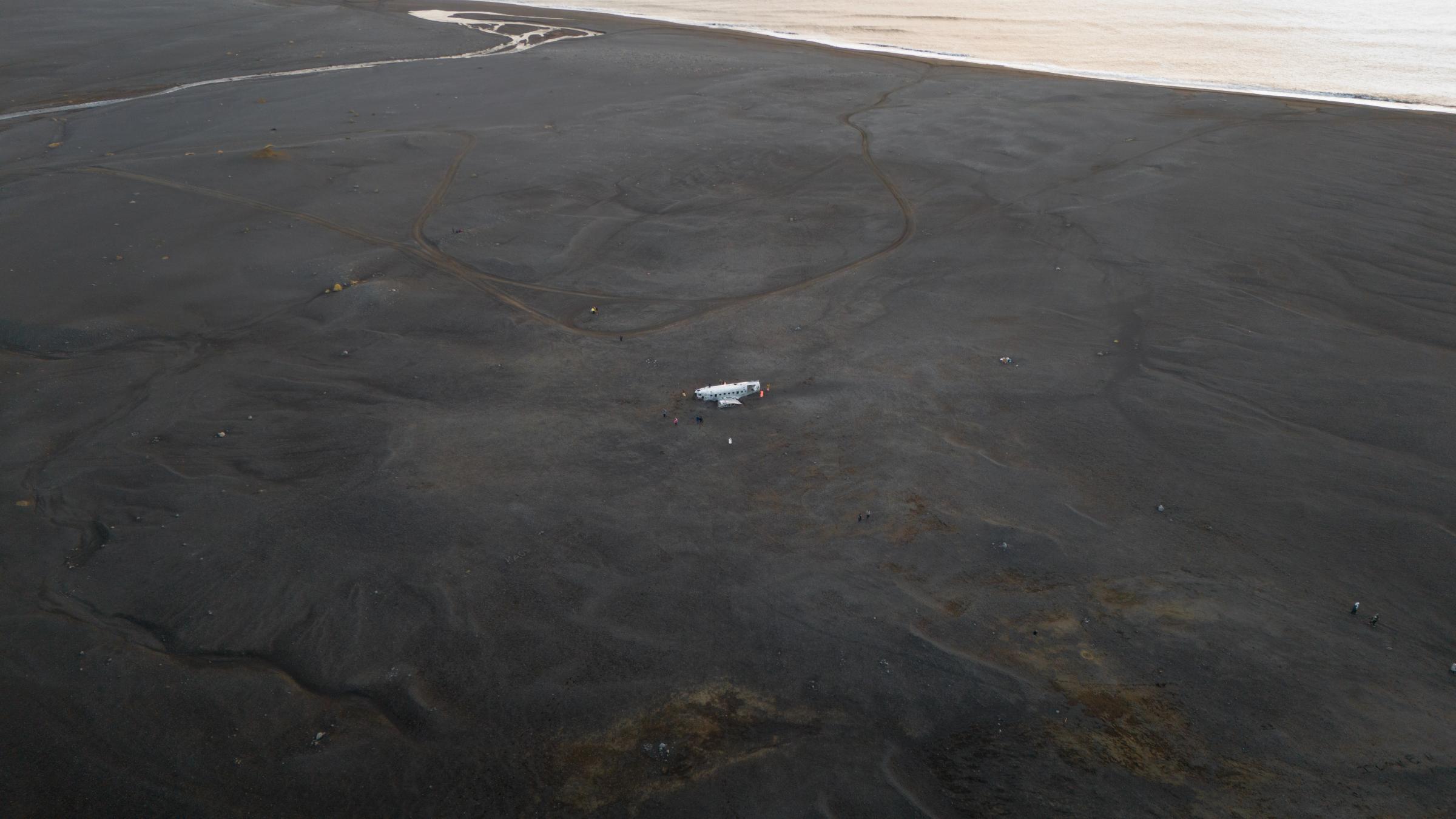 White plane wreck on a vast black sand plain by the water.