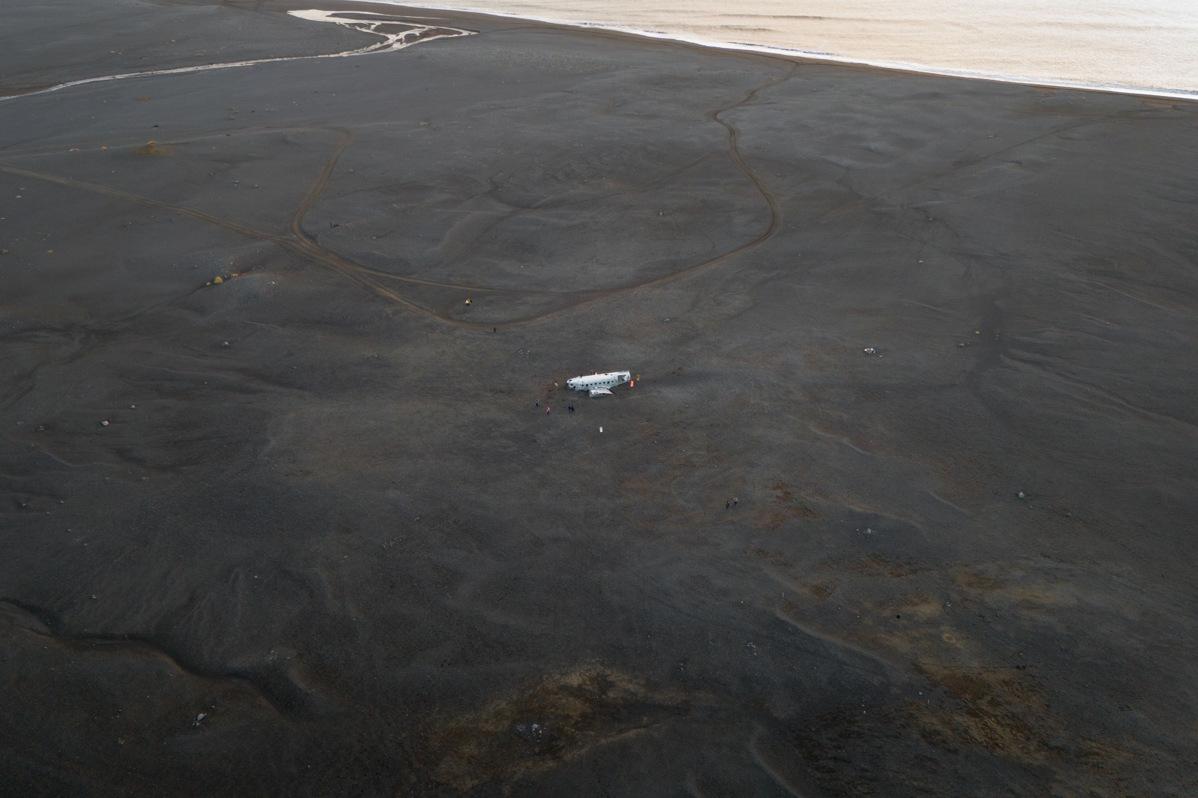 White plane wreck on a vast black sand plain by the water.