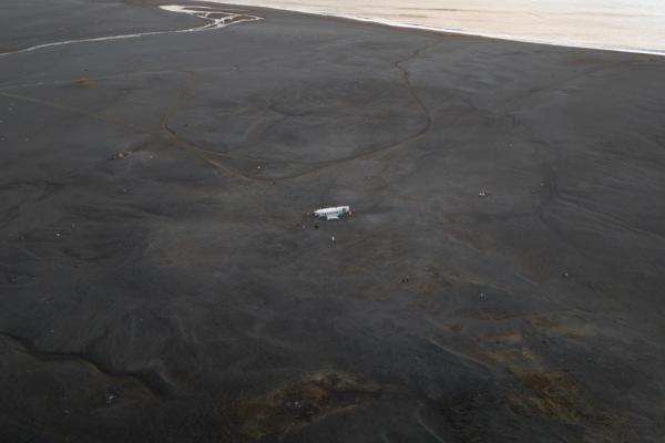 aerial view of a black sand beach with a plane wreck