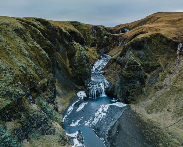 A river with waterfalls flows through a deep, moss-covered canyon.