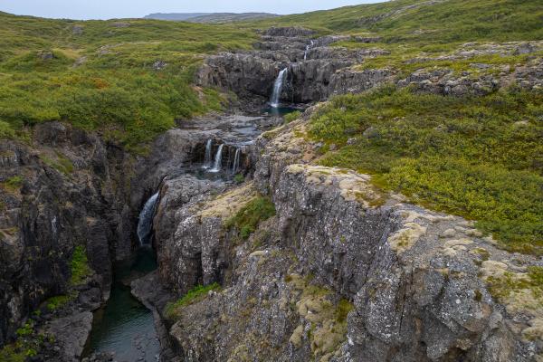 an aerial view of a waterfall in the middle of a canyon at vatnsfjordur iceland.