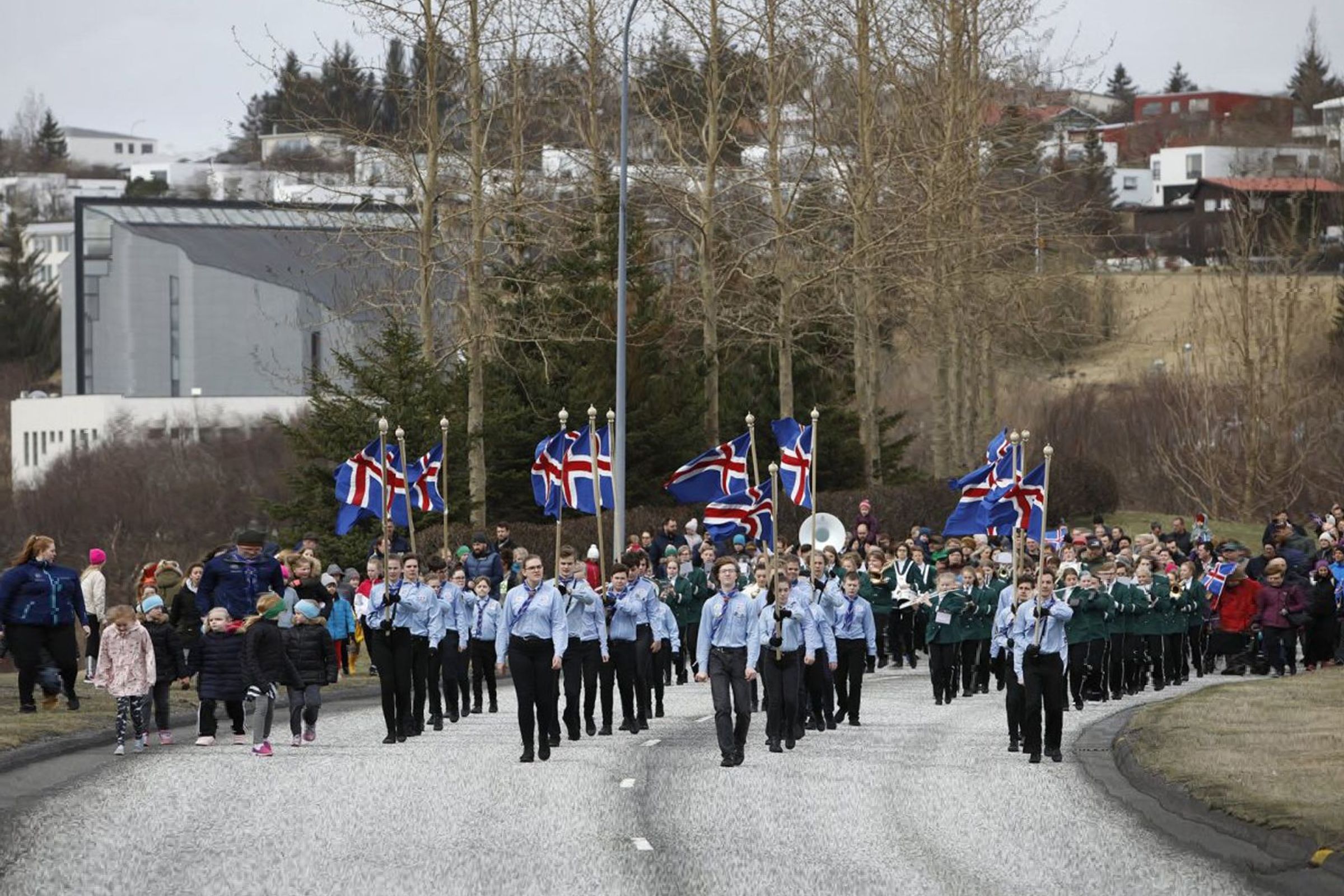 Sumardagurinn Fyrsti, Iceland a large group of people are marching down a street holding flags .