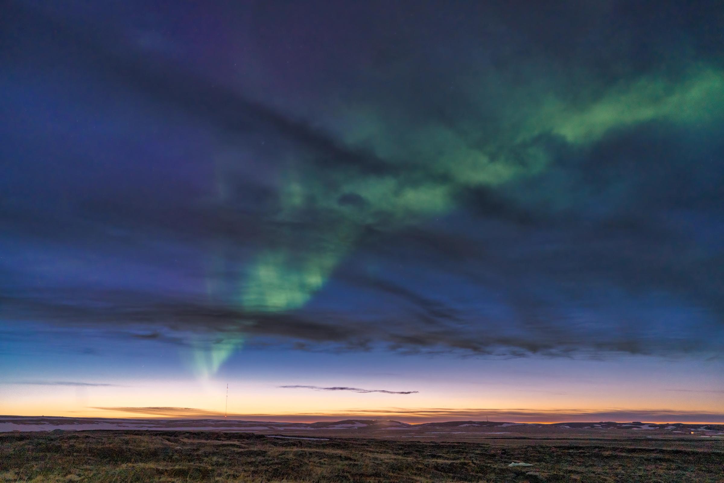 la aurora boreal está bailando en el cielo sobre un campo al atardecer.