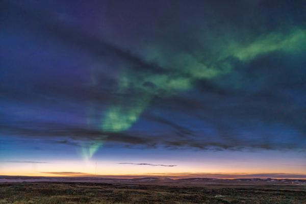 la aurora boreal está bailando en el cielo sobre un campo al atardecer.