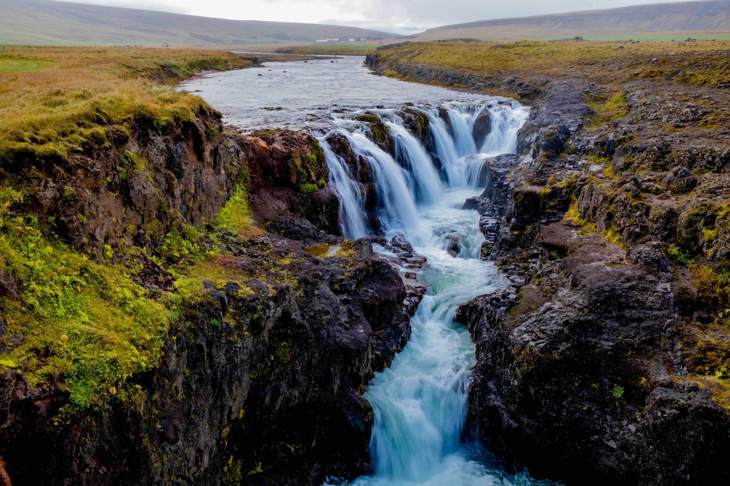 a waterfall is surrounded by rocks and grass in the middle of a river .