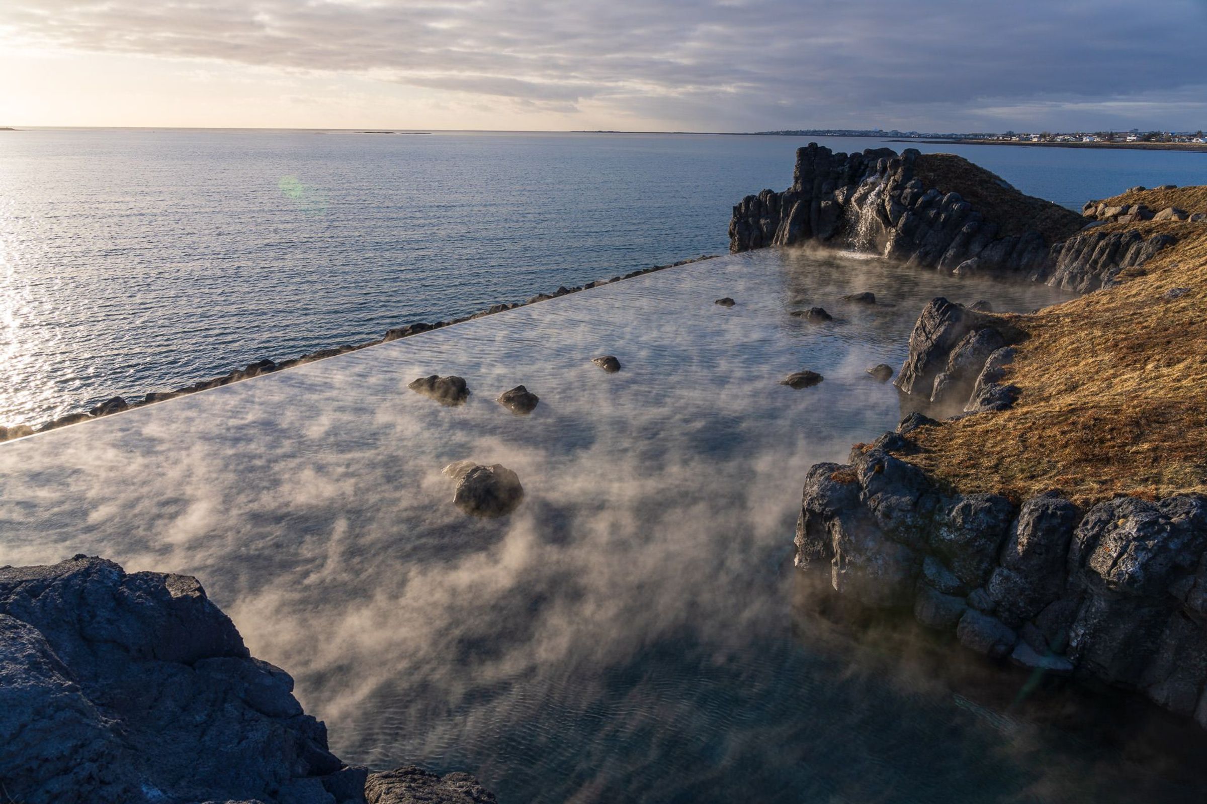 Steaming infinity geothermal pool with rocks, overlooking the ocean and rugged coast.