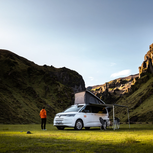 un hombre está de pie frente a una furgoneta camper con un toldo en la parte superior