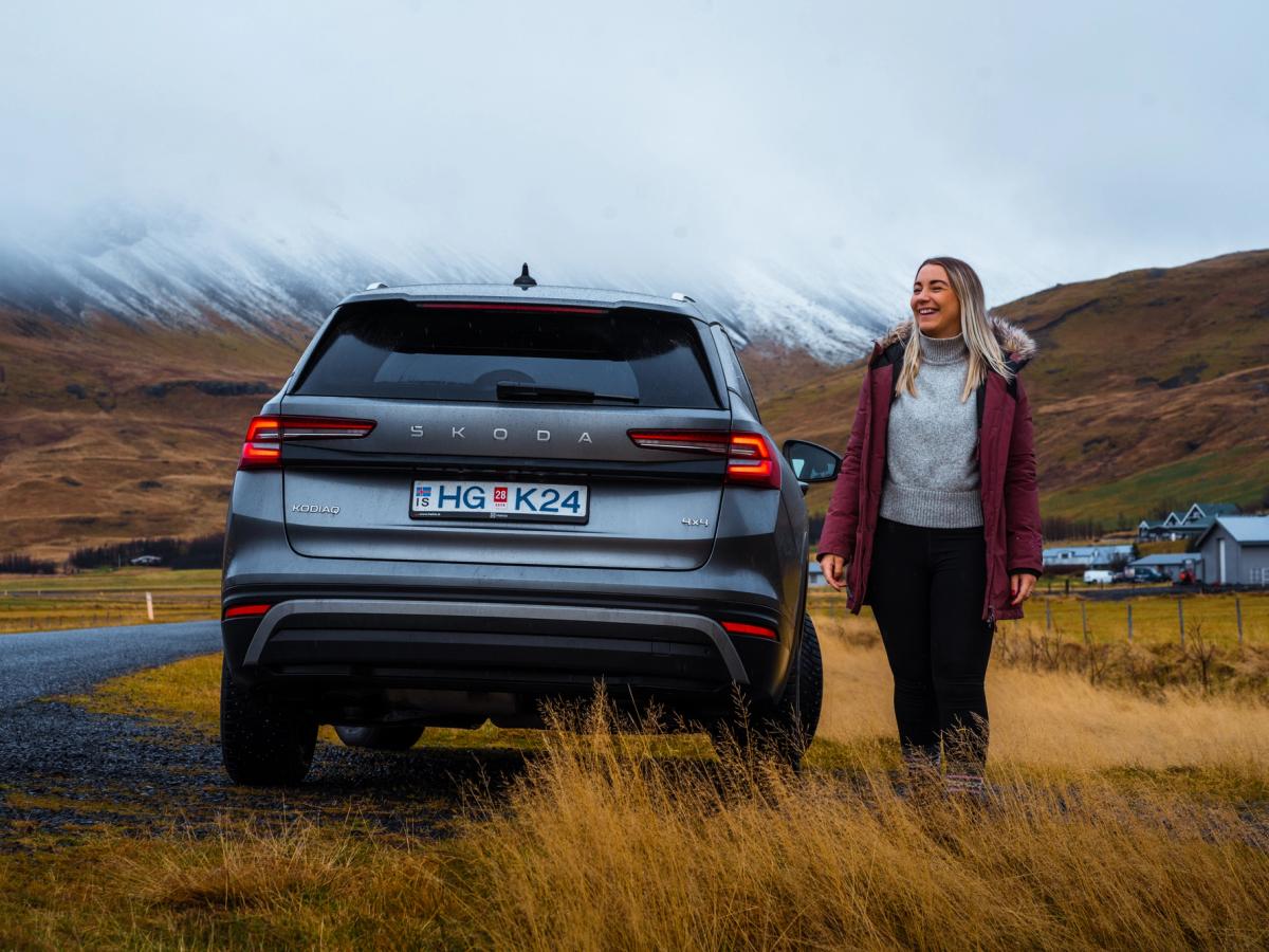 Pessoa vista por trás junto a um Skoda Kodiaq Vista traseira de um Skoda Kodiaq estacionado junto a uma estrada de cascalho, com uma pessoa por perto