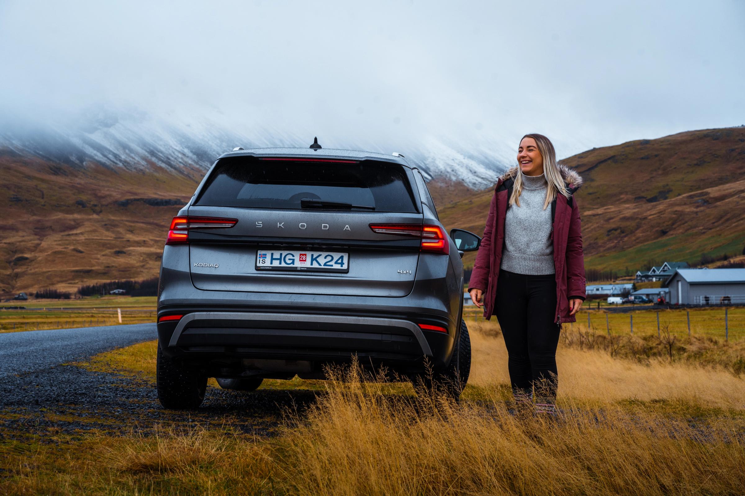 Pessoa vista por trás junto a um Skoda Kodiaq Vista traseira de um Skoda Kodiaq estacionado junto a uma estrada de cascalho, com uma pessoa por perto