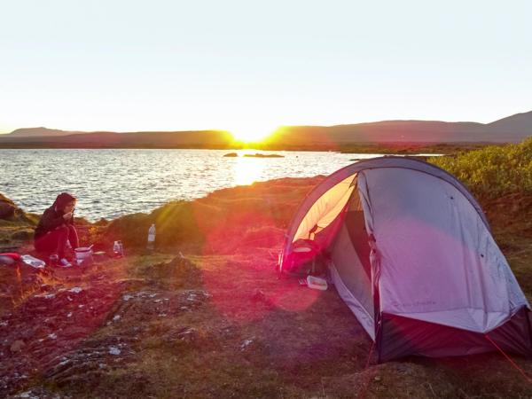 una persona comiendo junto a una tienda de campaña al lado de un lago al atardecer