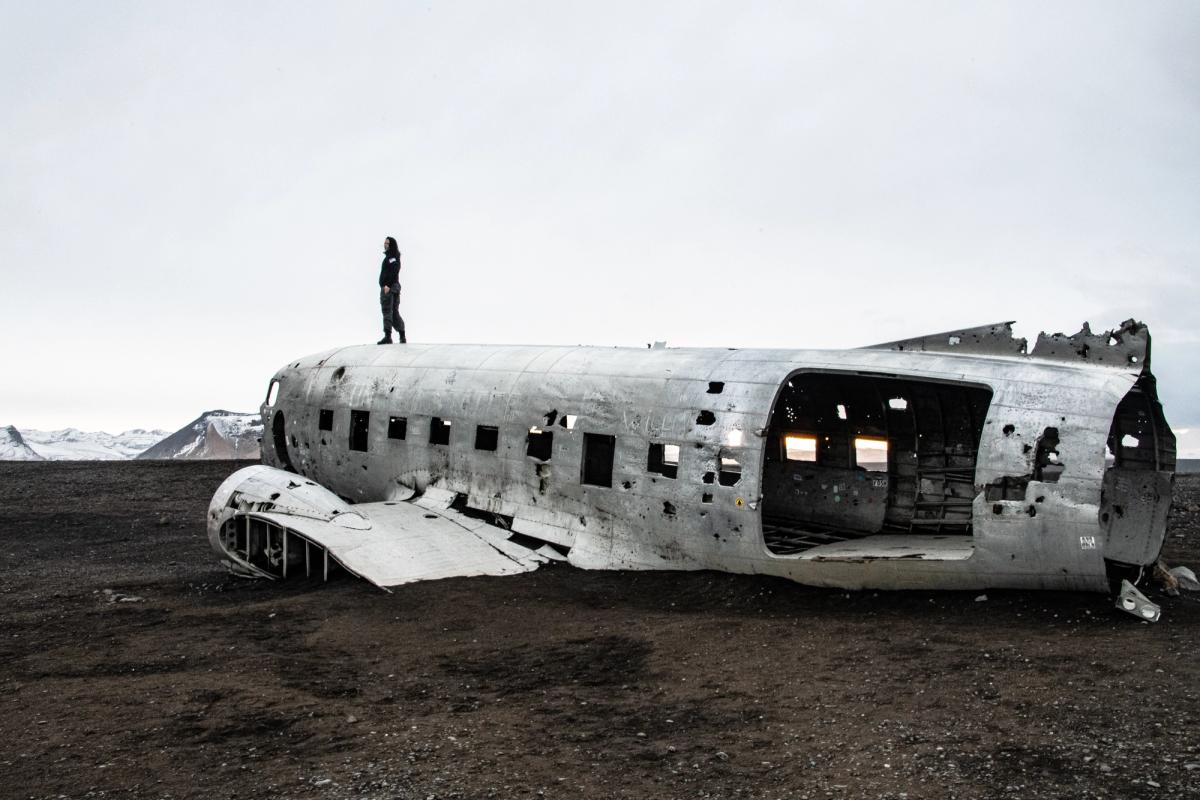 Una persona está parada sobre el fuselaje de un avión destrozado en un paisaje desolado y oscuro.