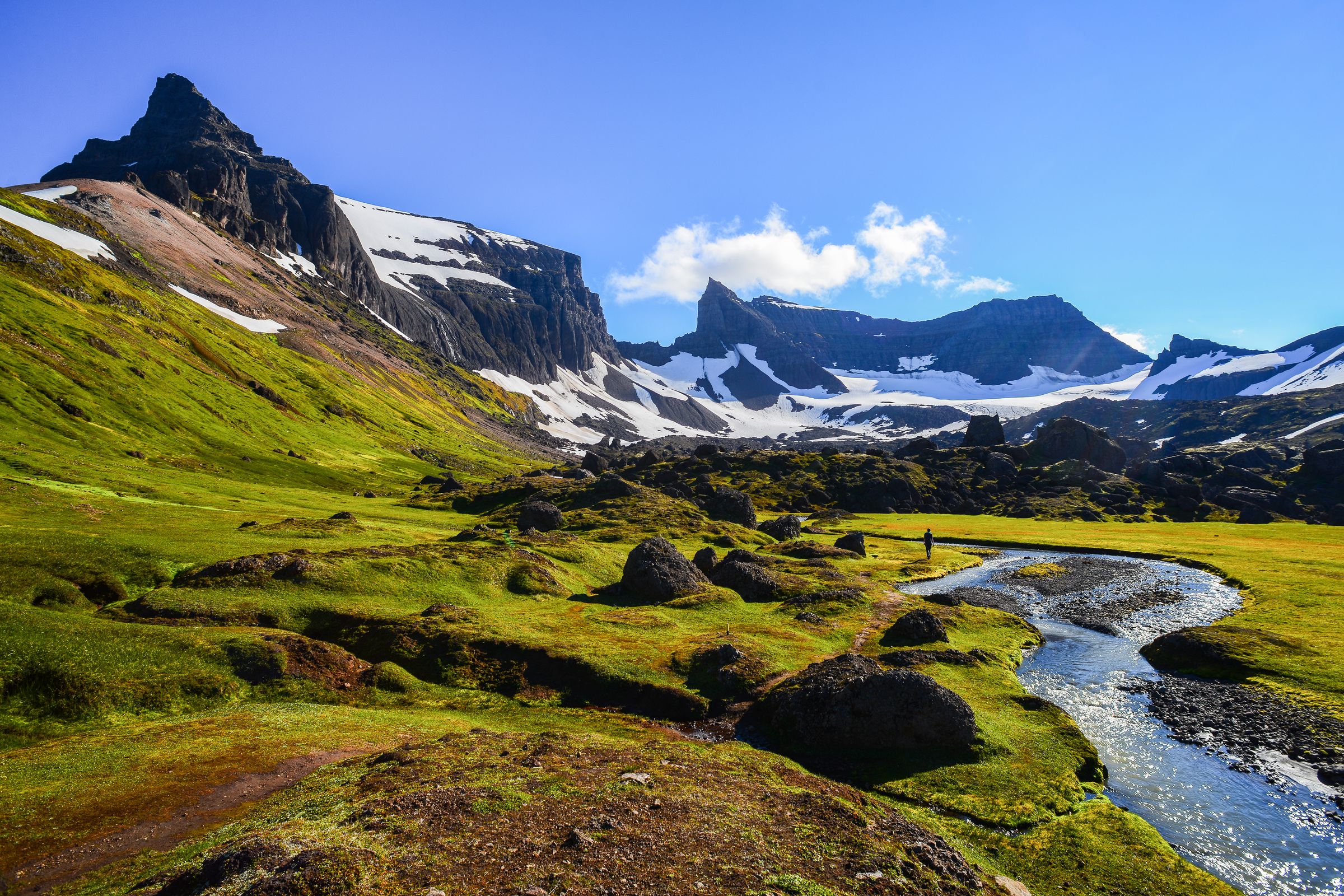 a person is standing on a bridge over a stream in the mountains at stórurð in east iceland.