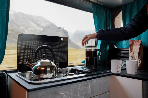 a person is pouring a cup of coffee into a french press inside a campervan