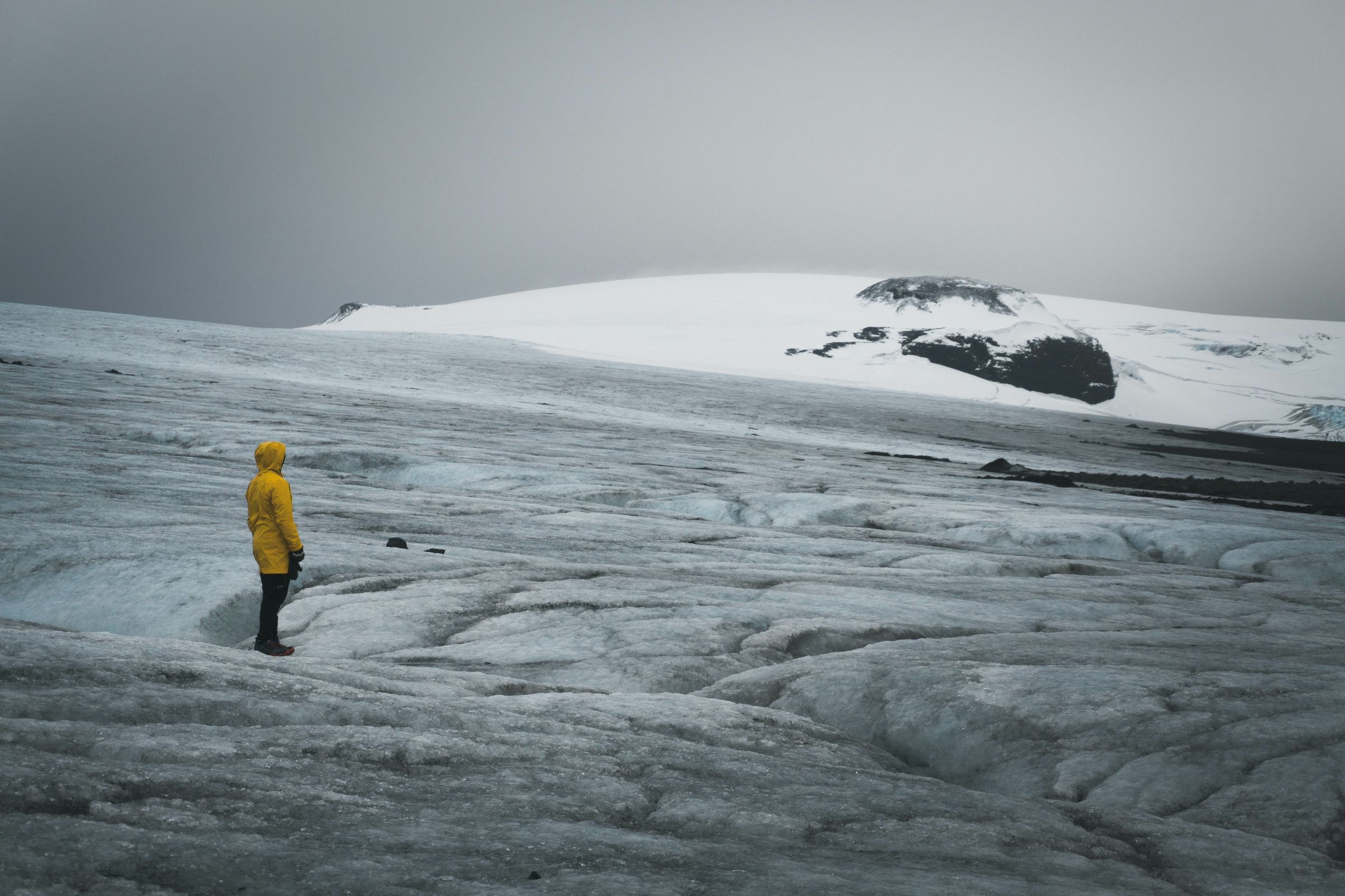 a person in a yellow raincoat is standing on top of a snow covered mountain at langjokull in iceland.