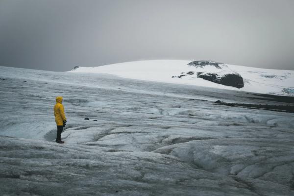 Une personne en imperméable jaune se tient au sommet d'une montagne enneigée à Langjökull en Islande.