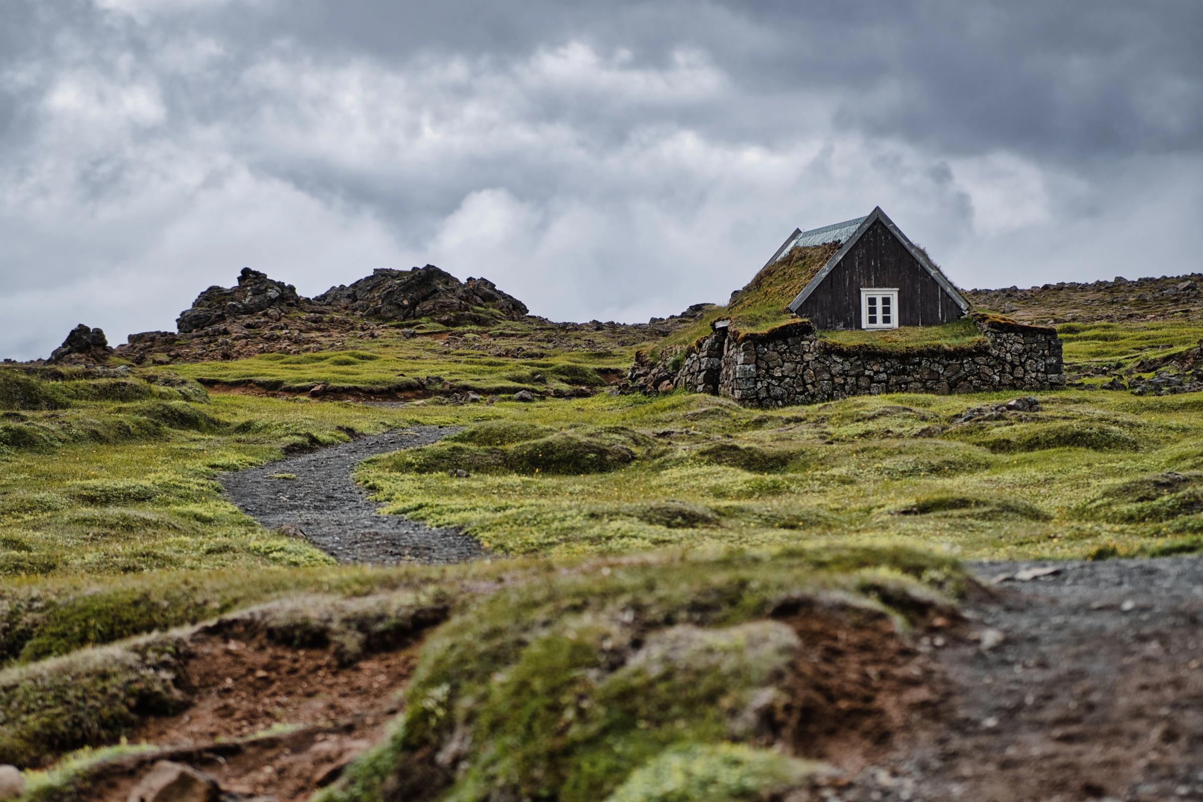 a small house with a green roof is sitting on top of a grassy hill .