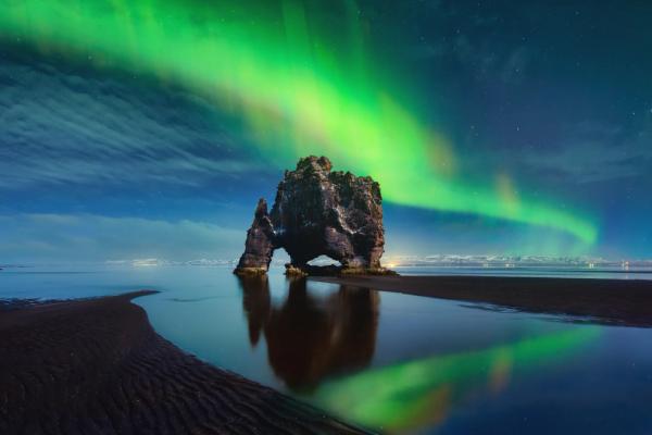 the aurora borealis is shining over a rock formation on the beach .
