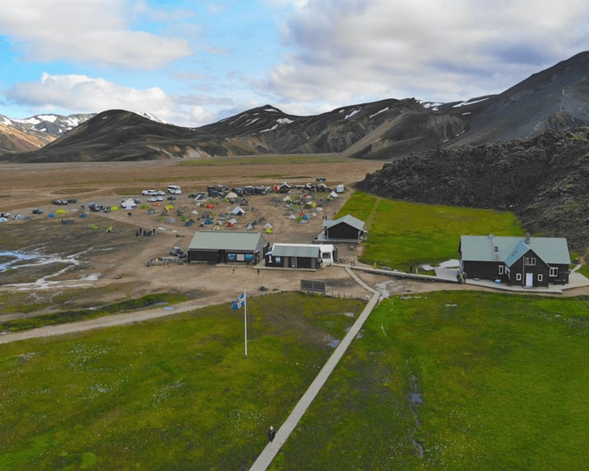 une vue aérienne d'un camping avec des tentes et des bâtiments au milieu d'un champ avec des montagnes en arrière-plan.