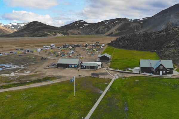une vue aérienne d'un camping avec des tentes et des bâtiments au milieu d'un champ avec des montagnes en arrière-plan.