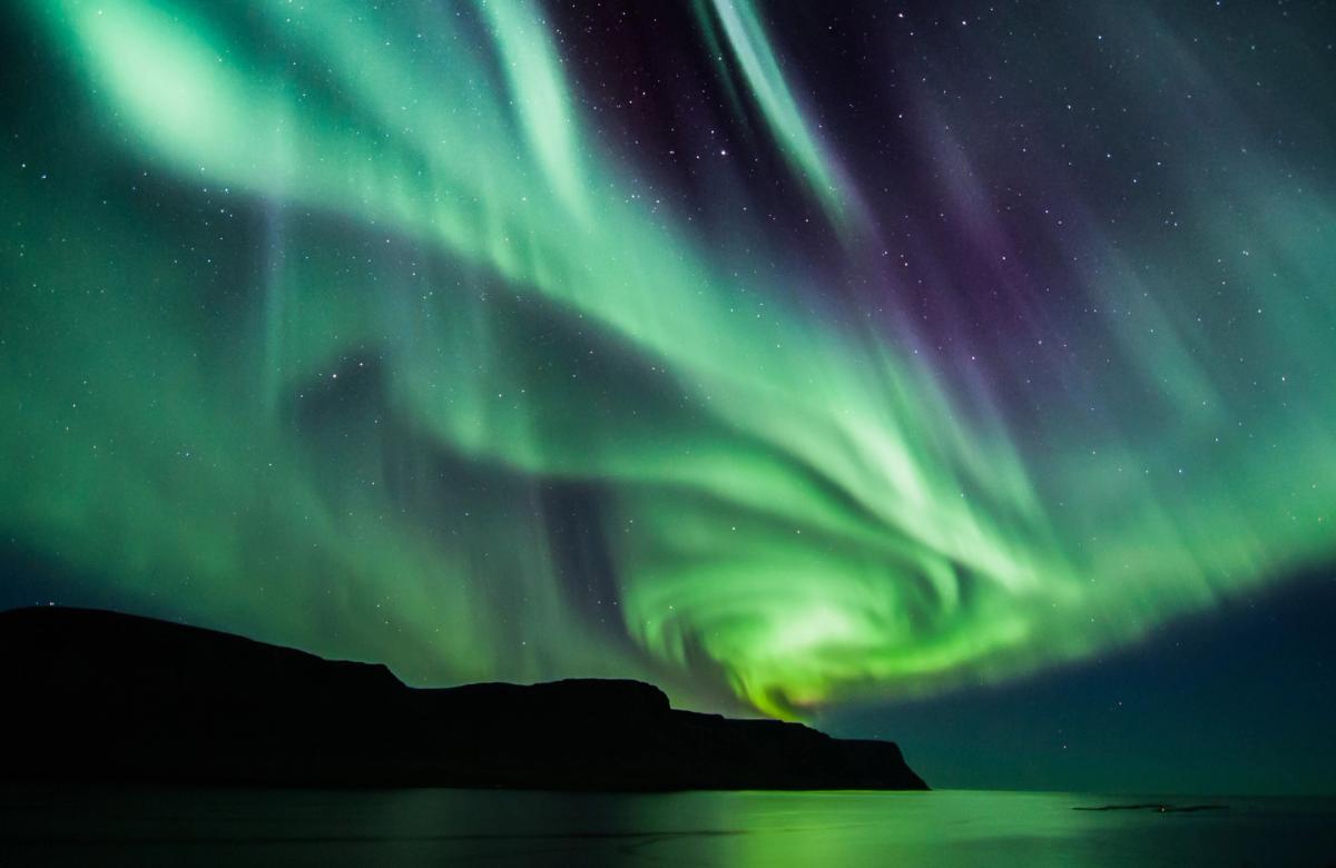 the aurora borealis is dancing in the night sky over the ocean in the west fjords in Iceland