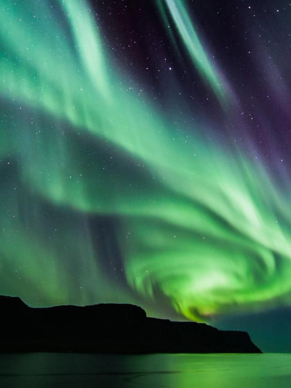 the aurora borealis is dancing in the night sky over the ocean in the west fjords in Iceland