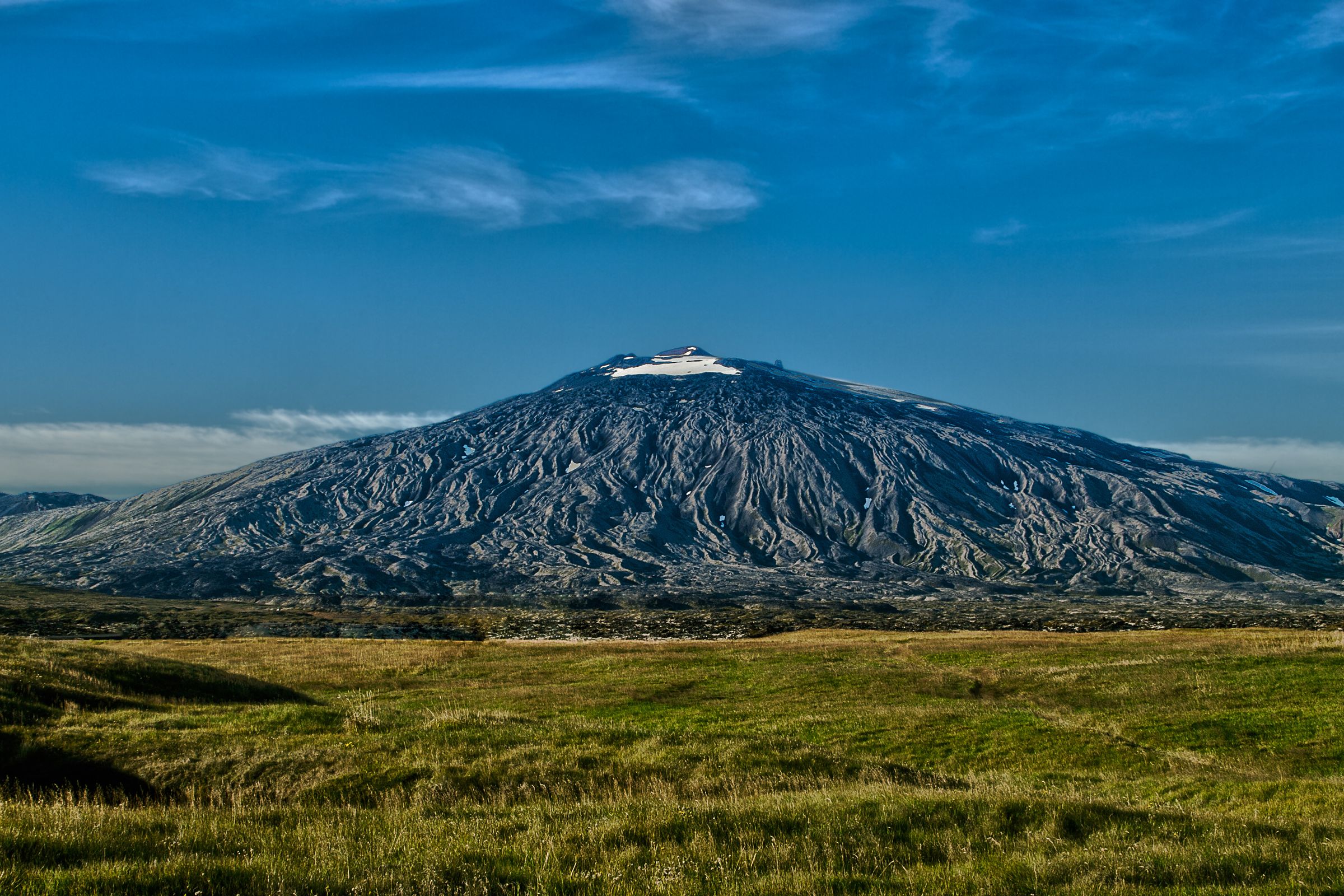 a mountain with snow on the top and a green grass field on the foreground