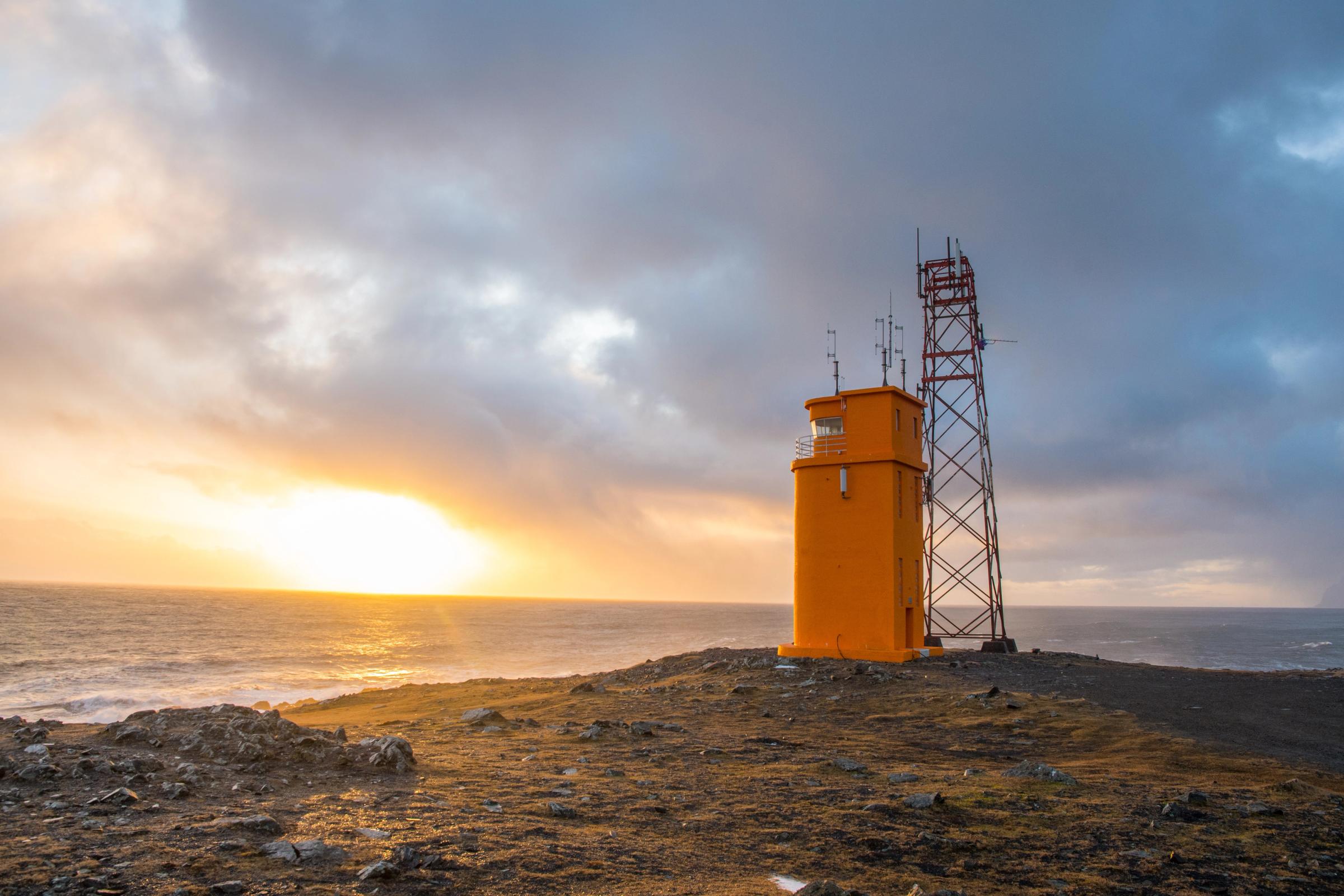 un faro en una colina con vista al océano al atardecer.