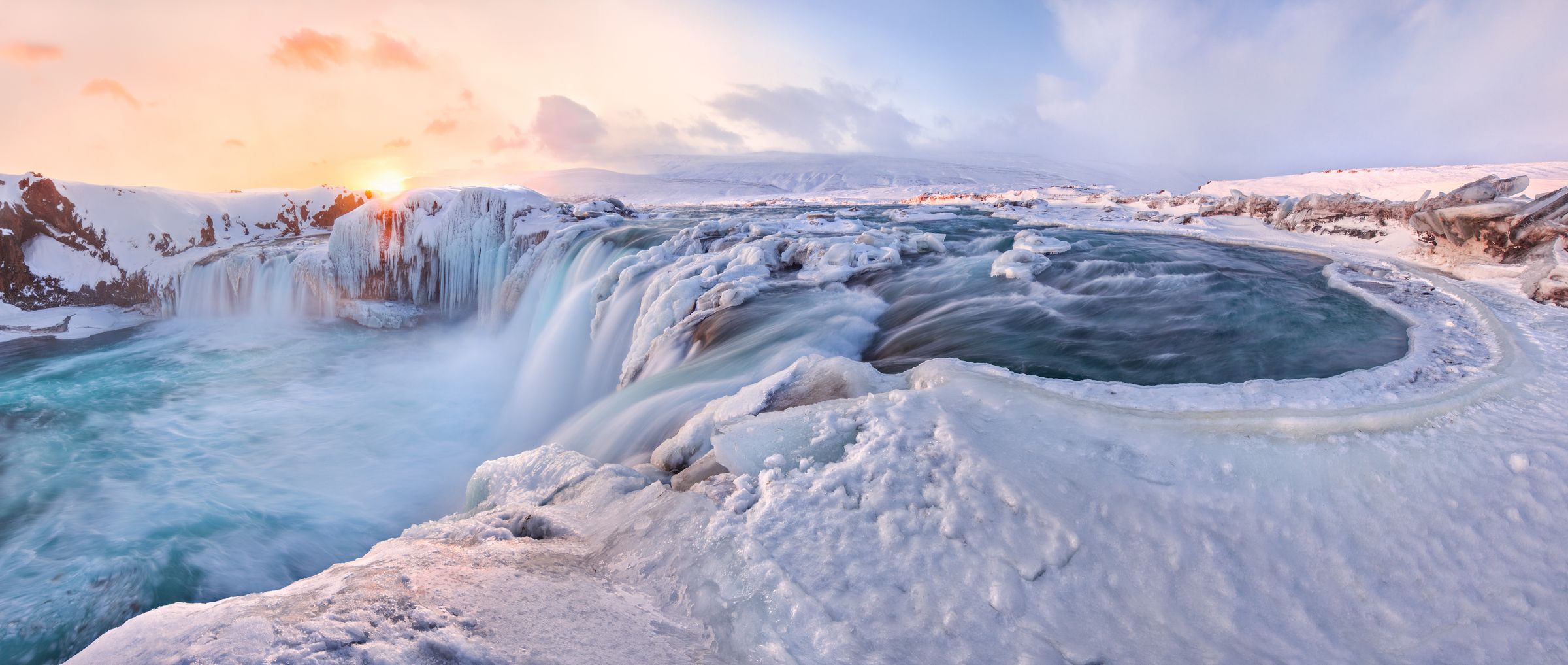 a waterfall surrounded by snow and ice with the sun shining through the clouds in iceland.