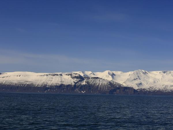 a large body of water with snow covered mountains in the background at skjálfandi bay in húsavik, Iceland.